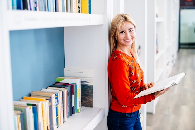 Fröhliche Frau in der Nähe von Bücherregal