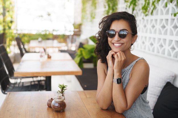 Fröhliche Frau in der Sonnenbrille, die in der Sommerterrasse des Cafés sitzt