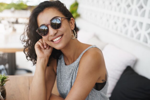 Fröhliche Frau in der Sonnenbrille, die in der Sommerterrasse des Cafés sitzt