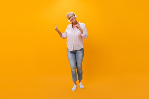 Fröhliche Frau in Kopfhörertänzen auf orangefarbenem Hintergrund
