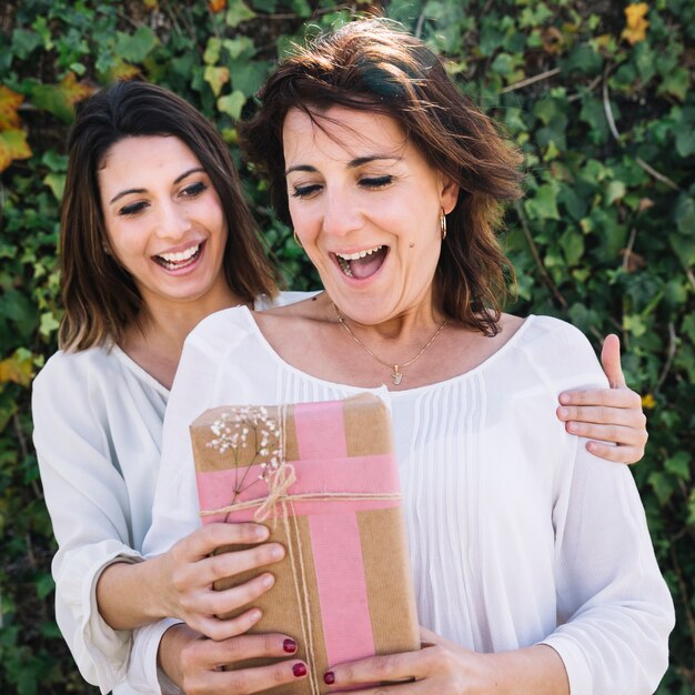 Fröhliche Frau schenkt einer Frau im Garten ein Geschenk