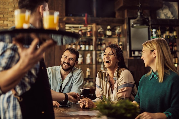 Kostenloses Foto fröhliche freunde, die spaß haben, während sie mit einem kellner in einem café sprechen