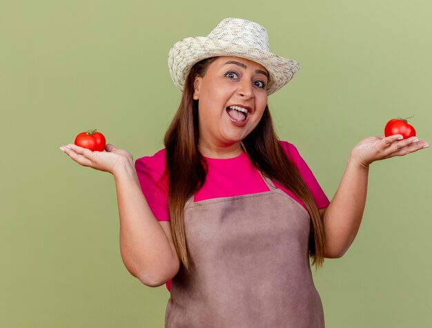 Fröhliche Gärtnerin mittleren Alters in Schürze und Hut, die frische Tomaten halten