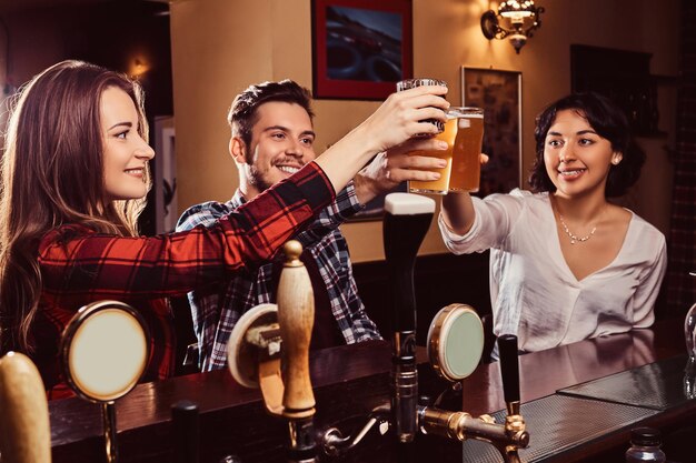 Fröhliche gemischtrassige Freunde, die mit Bier an der Bar oder im Pub anstoßen.