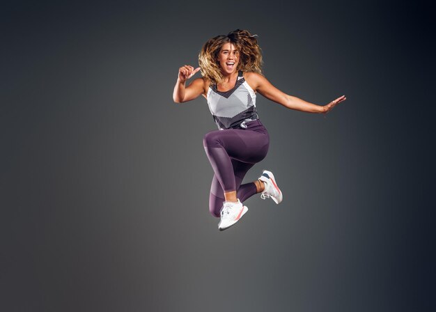 Fröhliche, glückliche Frau zeigt ihre Leistung im Fotostudio auf grauem Hintergrund.