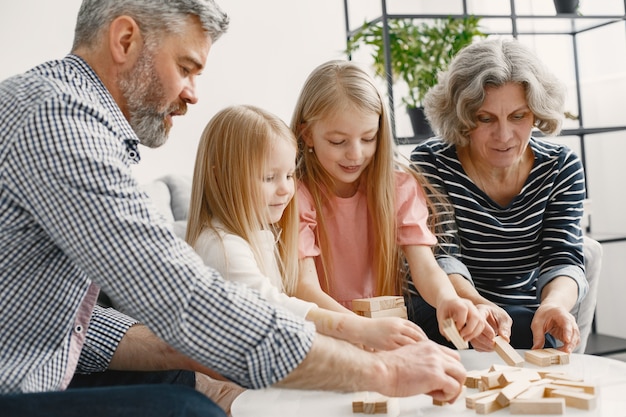 Fröhliche Großeltern und Enkel spielen zusammen Holzturm-Spielblöcke. Wohnzimmerinnenraum.