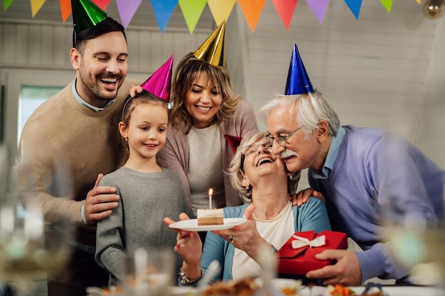 Fröhliche Großfamilie, die den Geburtstag der Seniorin feiert und sie mit einem Kuchen überrascht