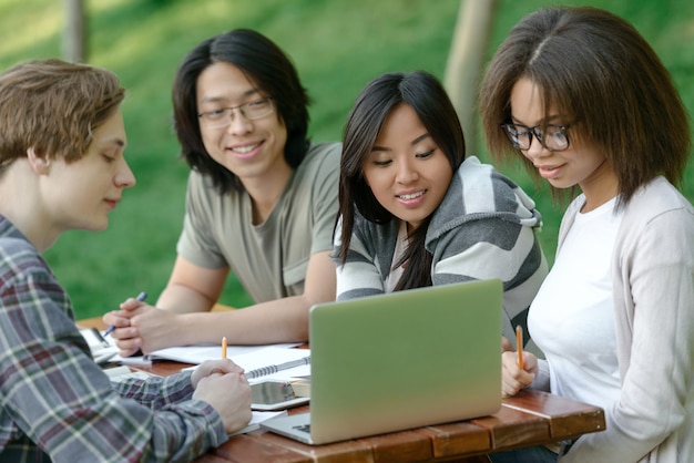 Fröhliche Gruppe junger Studenten, die sitzen und studieren