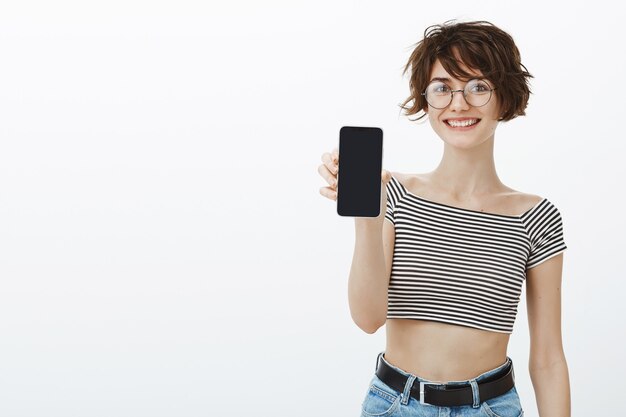 Fröhliche Hipster-Frau stellen Anwendung vor, Smartphonebildschirm zeigend