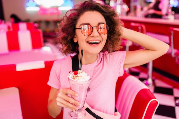 Fröhliche, hübsche, stilvolle lächelnde Frau im Retro-Vintage-Café der 50er Jahre, die am Tisch sitzt