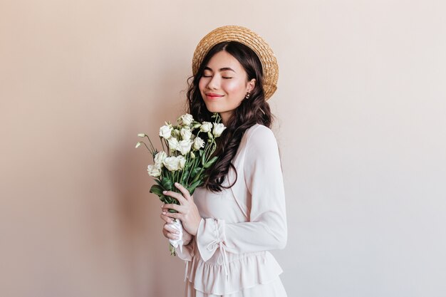 Fröhliche japanische Frau, die Blumen hält. Studioaufnahme des stilvollen asiatischen Modells im Strohhut mit Blumenstrauß.