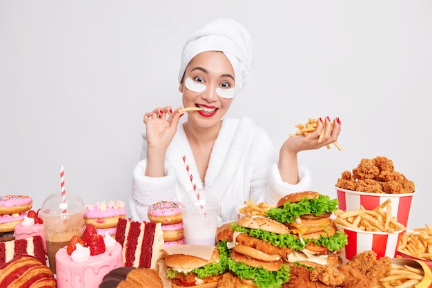 Fröhliche junge Asiatin isst köstliche appetitanregende französische Freundin hat schlechte Essgewohnheiten