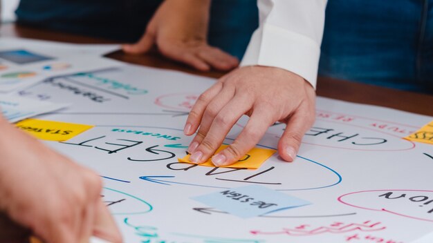 Fröhliche junge asiatische Geschäftsleute und Geschäftsfrauen, die Brainstorming-Ideen über ein neues Papierkram-Projekt treffen