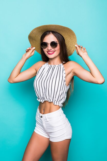 Fröhliche junge attraktive Frau in Sonnenbrille und Hut auf türkisfarbenem Hintergrund