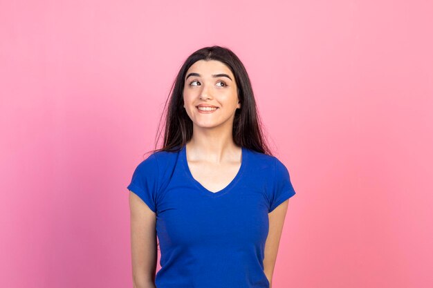 Fröhliche junge Dame, die auf rosa Hintergrund steht und nach draußen schaut Hochwertiges Foto