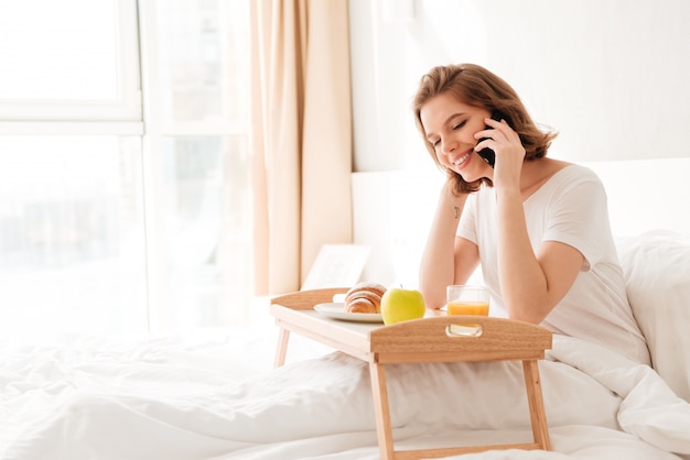 Fröhliche junge Dame, die drinnen mit Croissanttrinksaft sitzt