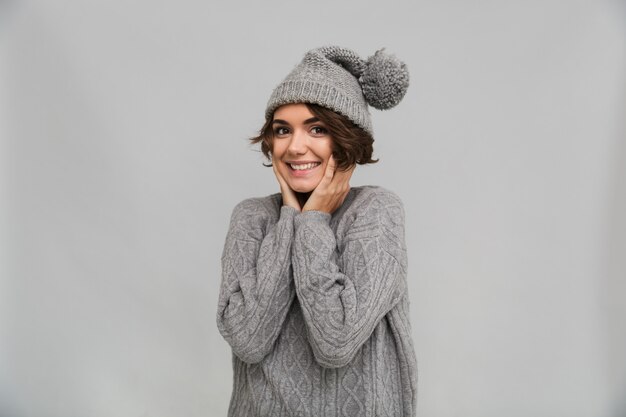 Fröhliche junge Dame in Pullover und warmem Hut gekleidet
