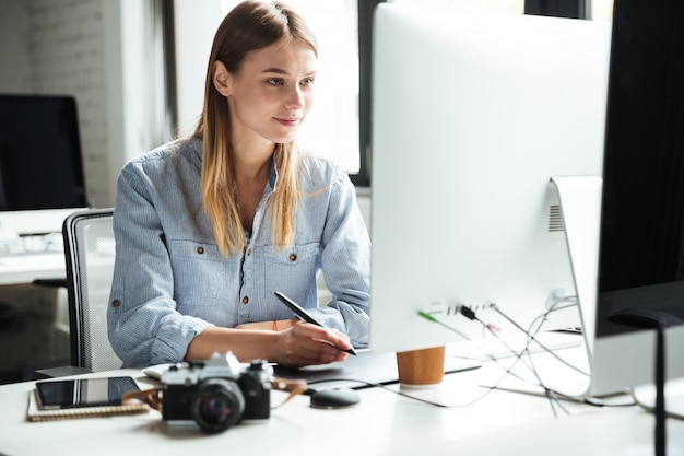 Fröhliche junge Frau arbeiten im Büro mit Computer