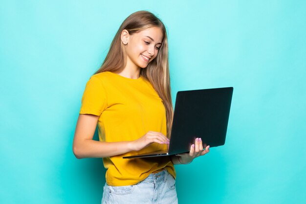 Fröhliche junge Frau, die am Laptop arbeitet, der lokal auf türkisfarbener Wand aufwirft