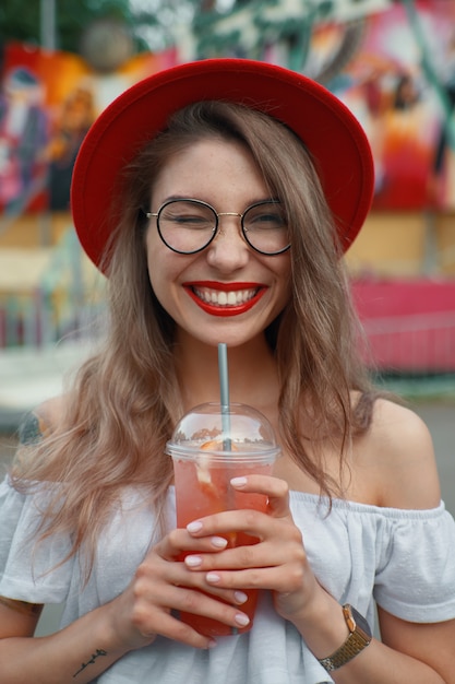Fröhliche junge Frau, die einen Drink beim Lächeln hält
