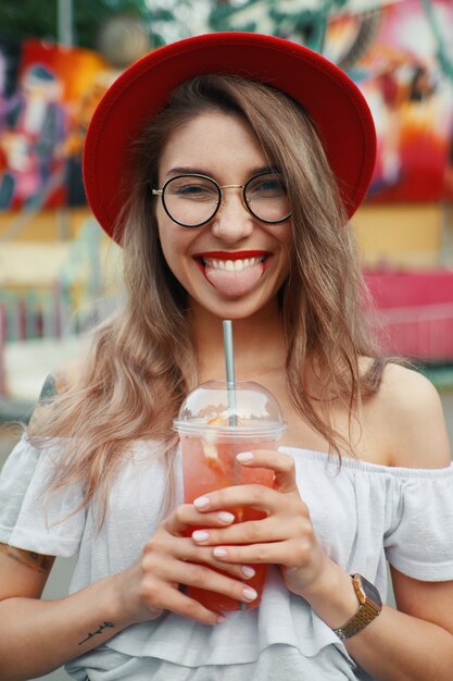 Fröhliche junge Frau, die einen Drink beim Lächeln hält