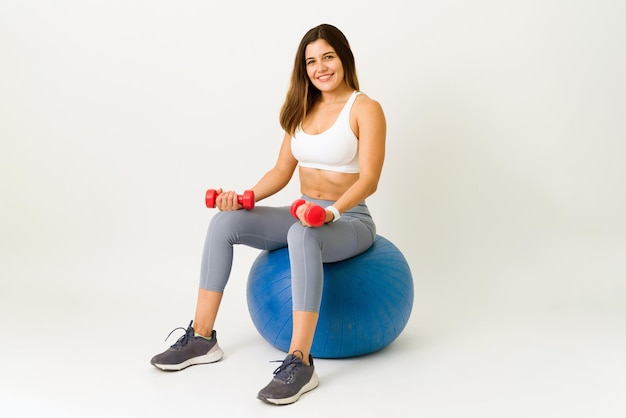 Fröhliche junge Frau, die lächelt und Augenkontakt herstellt, während sie auf einem Fitnessball sitzt. Schöne Frau, die sich von einem Training ausruht