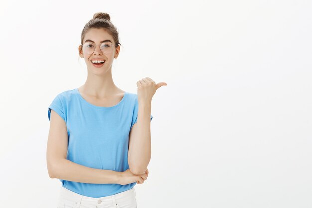 Fröhliche junge Frau, die lächelt, Weg zeigt und Finger direkt auf Werbung zeigt
