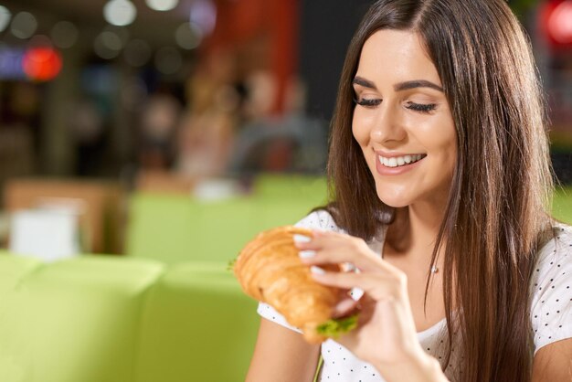 Fröhliche junge Frau, die leckeren Snack im Café genießt