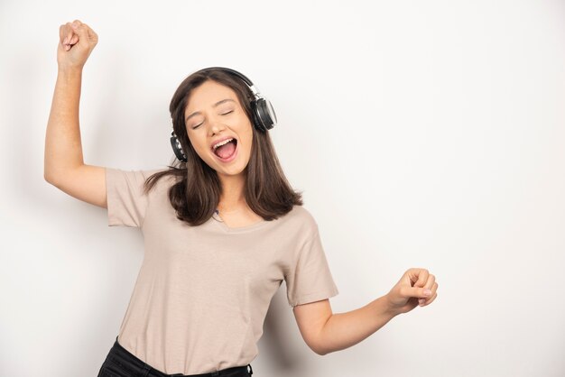 Fröhliche junge Frau im beigen Hemd, die Musik in den Kopfhörern tanzt und hört.