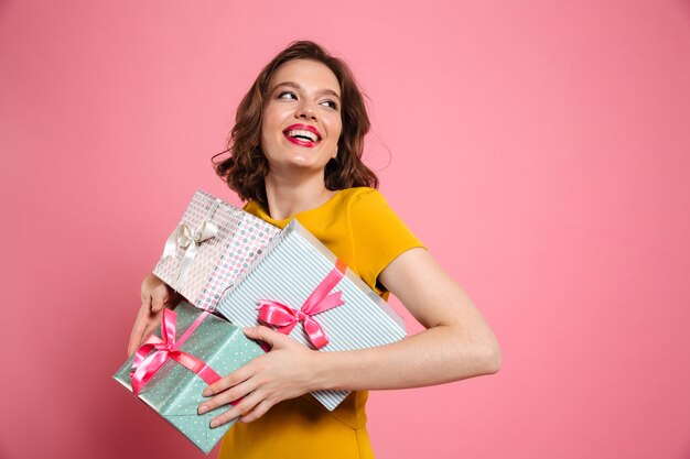 Fröhliche junge Frau im gelben Kleid, das Haufen von Geschenken hält