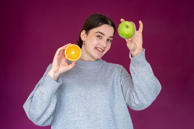 Fröhliche junge Frau mit Apfel und Orange auf lila Hintergrund