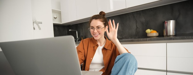 Fröhliche junge Frau mit Brille sagt Hallo, winkt mit der Hand am Laptop und spricht mit einem Freund Online-Video