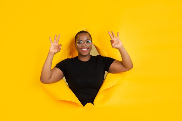Fröhliche junge Frau posiert in einem zerrissenen gelben Papierloch