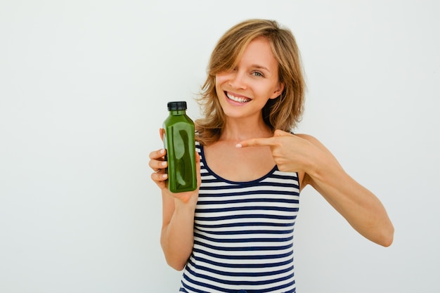 Fröhliche junge Frau zeigt auf grüne Flasche