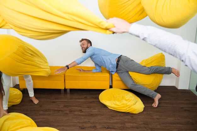 Fröhliche junge Mann auf der Couch unter fliegenden beanbags