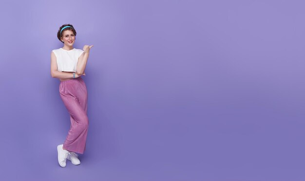 Fröhliche junge Teenager-Frau, die mit ihrem Finger zeigt, isoliert auf lila Hintergrund mit Kopier-Spa