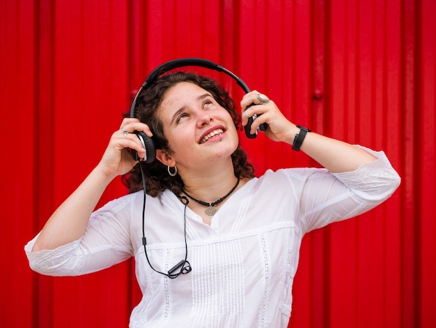 Fröhliche kaukasische Frau, die Musik mit Kopfhörern auf rotem Hintergrund hört