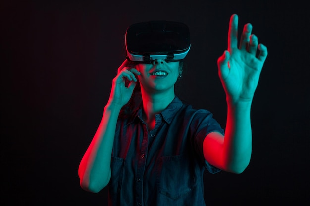 Fröhliche kaukasische Frau, die sich mit Virtual-Reality-Helm im Studio amüsiert. Futuristische Brille für die virtuelle Realität, die von einer schönen Frau verwendet wird.