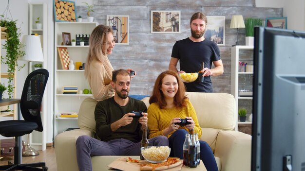 Fröhliche kaukasische Freunde, die Videospiele auf dem großen Fernseher im Wohnzimmer spielen.