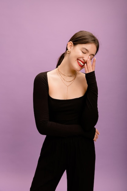 Fröhliche kaukasische junge Dame mit roten Lippen schloss die Augen in schwarzer Kleidung auf violettem Hintergrund Lifestyle verschiedene Emotionen Freizeitkonzept