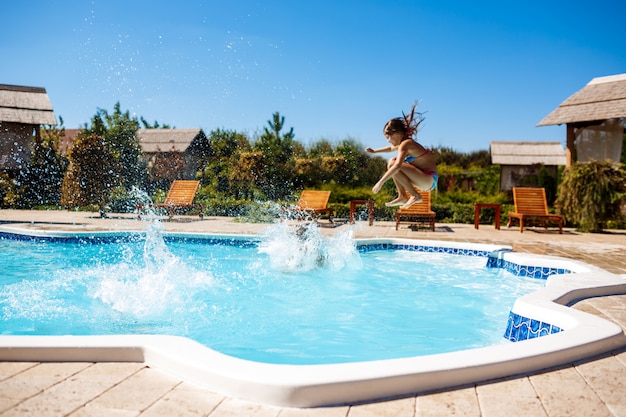 Fröhliche Kinder freuen sich, springen, schwimmen im Pool.