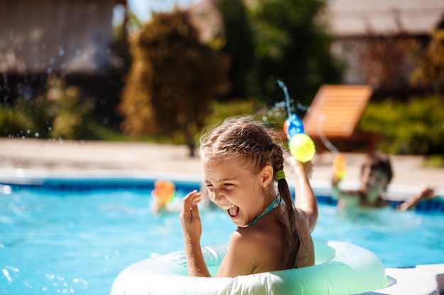 Fröhliche Kinder spielen Wassergewehre, freuen sich, springen, schwimmen im Pool.