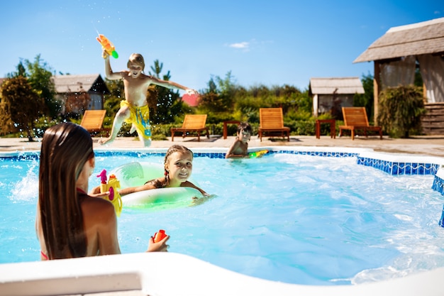 Fröhliche Kinder spielen Wassergewehre, freuen sich, springen, schwimmen im Pool.