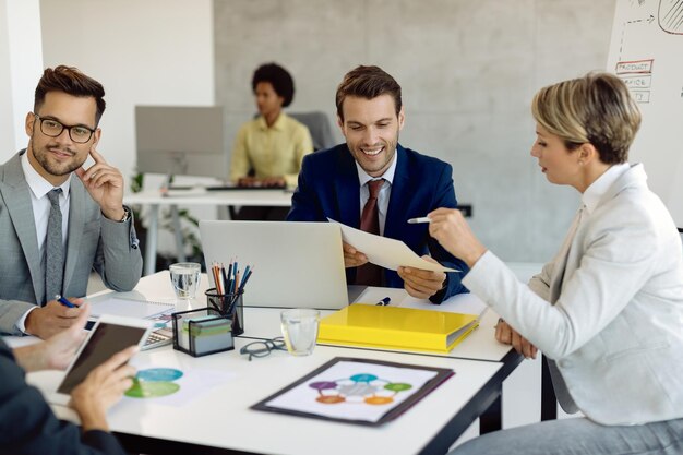 Fröhliche Kollegen, die zusammenarbeiten, während sie Geschäftsberichte bei einem Meeting im Büro analysieren