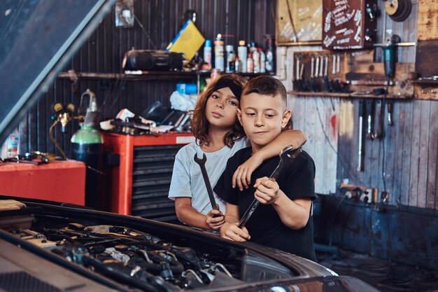 Fröhliche, lustige Kinder versuchen, ein kaputtes Auto bei einem geschäftigen Autoservice zu reparieren.