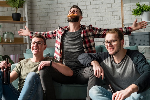 Fröhliche männliche Freunde, die Pizza und Bier haben und Sport im Fernsehen schauen