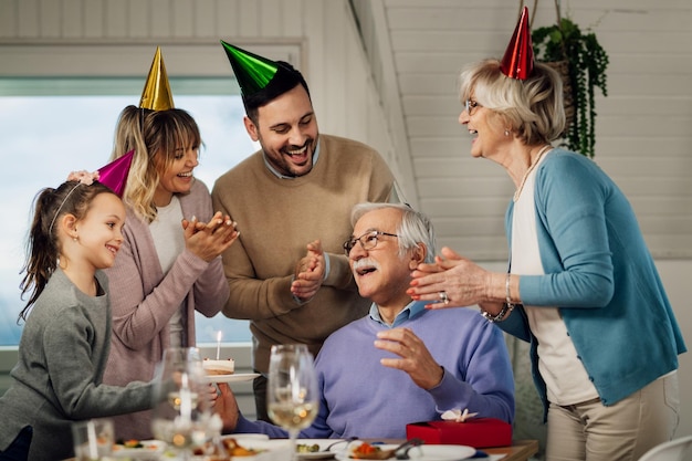 Fröhliche Mehrgenerationenfamilie, die singt, während sie den Geburtstag eines älteren Mannes im Speisesaal feiert