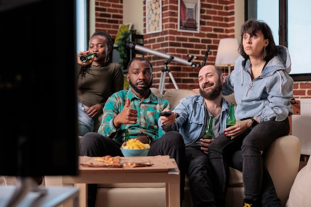 Kostenloses Foto fröhliche menschen, die fernsehsendungen oder filme im fernsehen ansehen und sich zu hause versammeln. bierflaschen trinken und snacks essen, film im fernsehprogramm anschauen, unterhaltung.