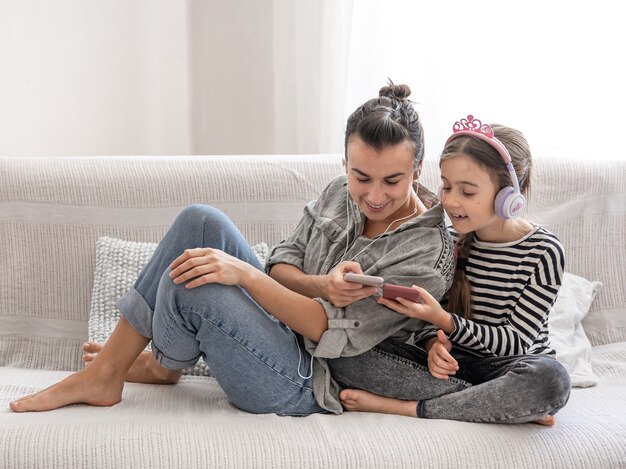 Fröhliche Mutter und Tochter ruhen sich zu Hause aus und hören Musik über Kopfhörer. Das Konzept einer glücklichen Familie und freundschaftlicher Beziehungen.