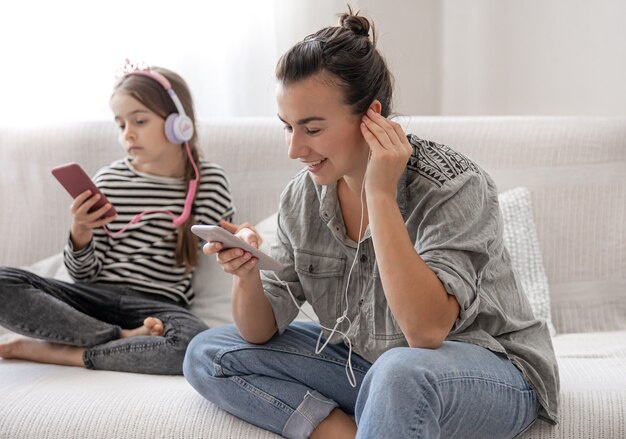 Fröhliche Mutter und Tochter ruhen sich zu Hause aus und hören Musik über Kopfhörer